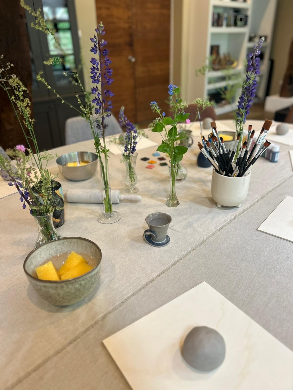 De werktafel klaargezet met klei, penselen en veldbloemen